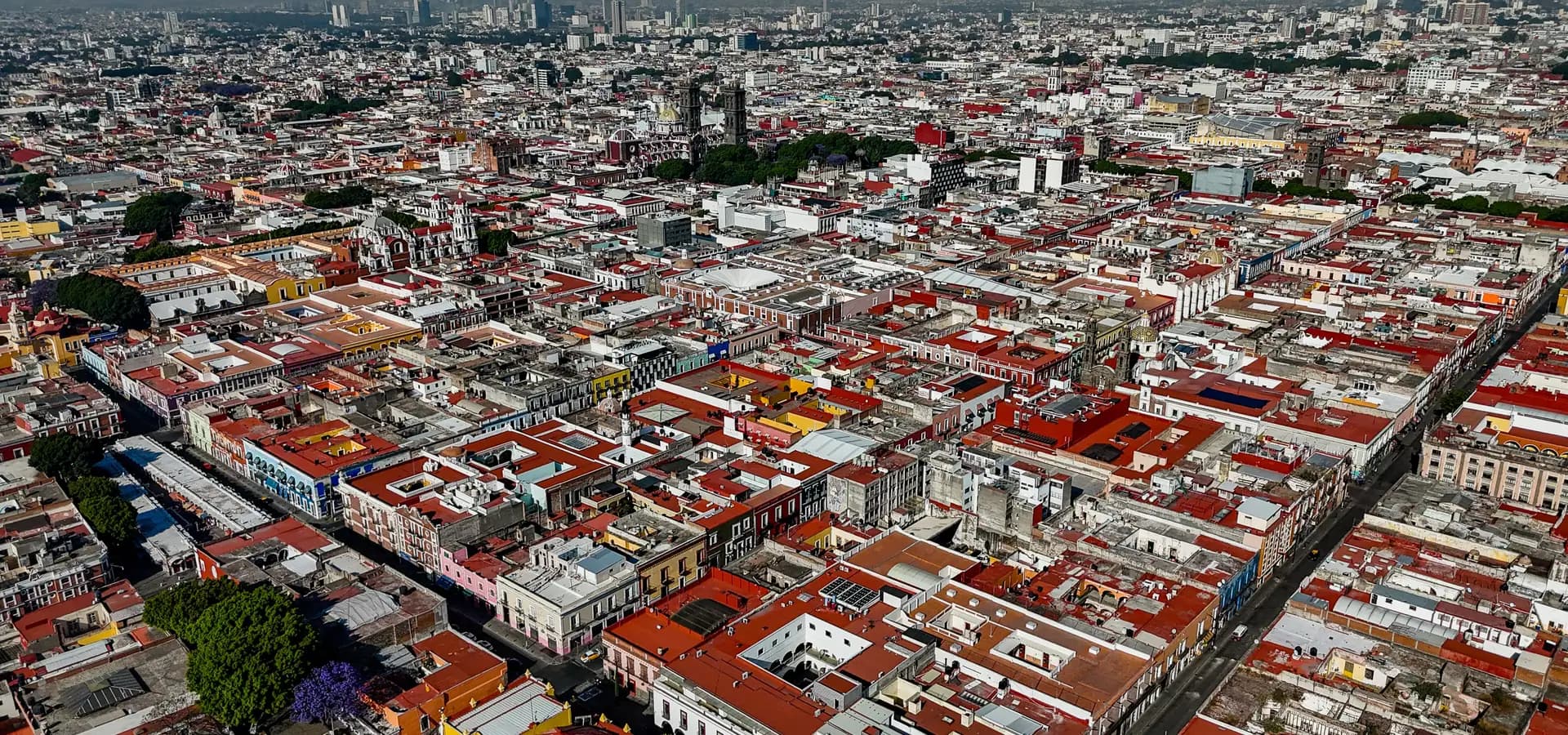 Aerial view of Puebla's historic center, red rooftops in a street grid with the cathedral towers and high-rises beyond