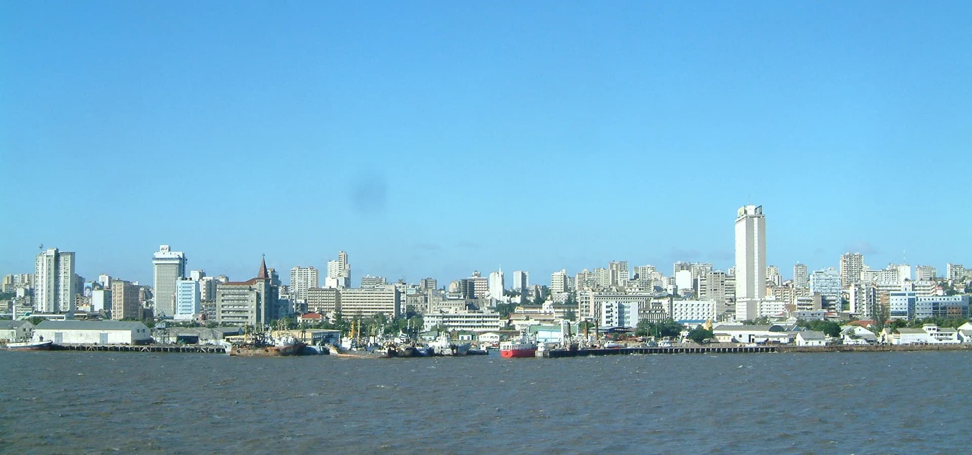Maputo skyline of white towers and port warehouses seen across the bay under a clear blue sky