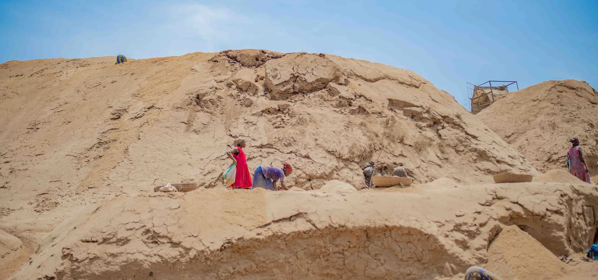Enormes montes claros de casca de arroz como dunas de deserto na Abakaliki Rice Mill, com figuras pequenas trabalhando sob um céu azul