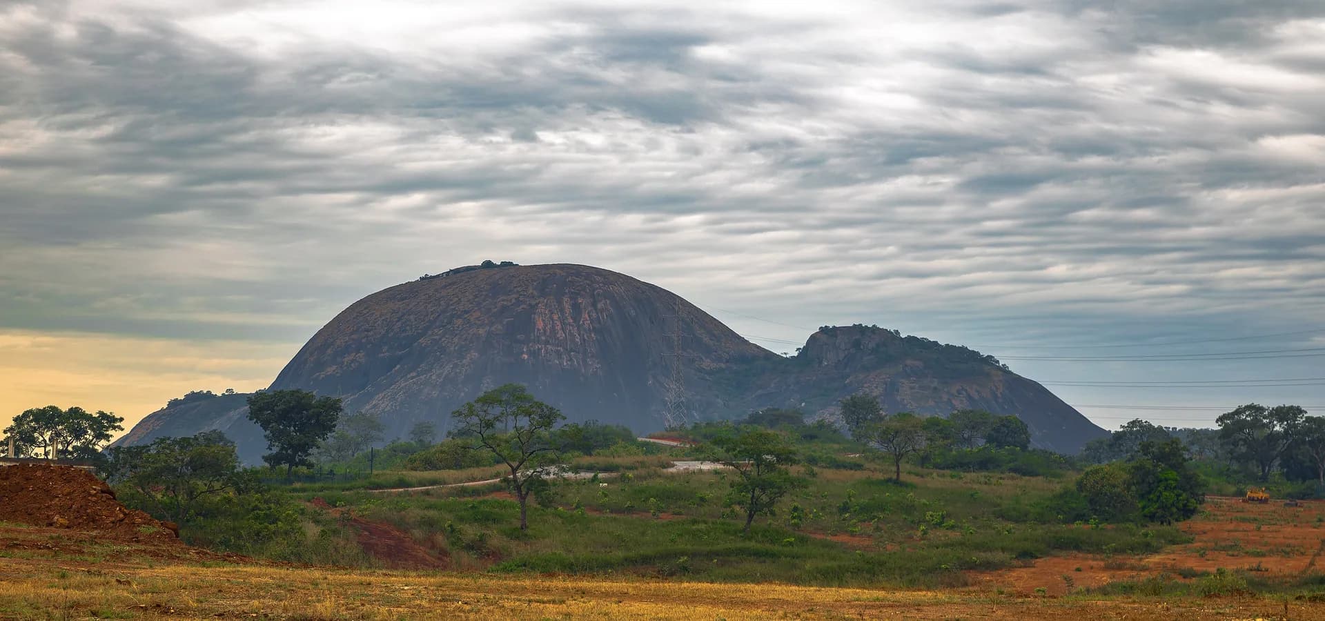 Die kahle Granitkuppel des Aso Rock erhebt sich über grüner Savanne und roter Erde am Rand von Abuja