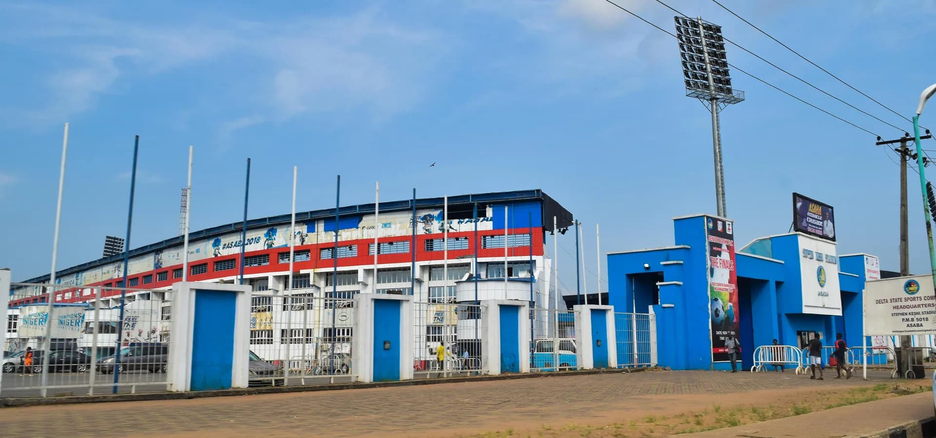 Estádio Stephen Keshi, vermelho, branco e azul, em Asaba, com refletores sob um amplo céu azul