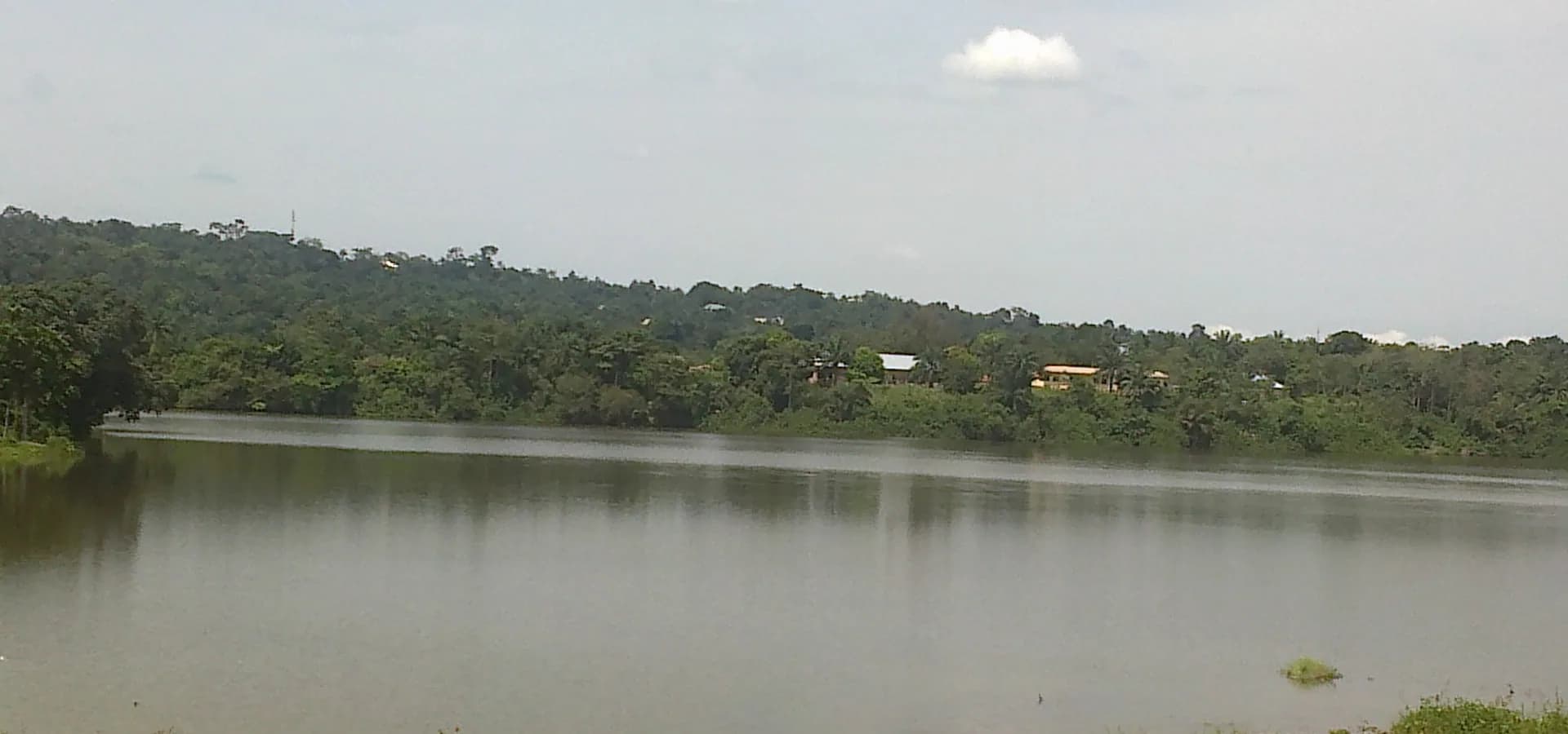 Das stille Wasser des Agulu-Sees bei Awka, umrahmt von grünen bewaldeten Hügeln und einem blassen Himmel