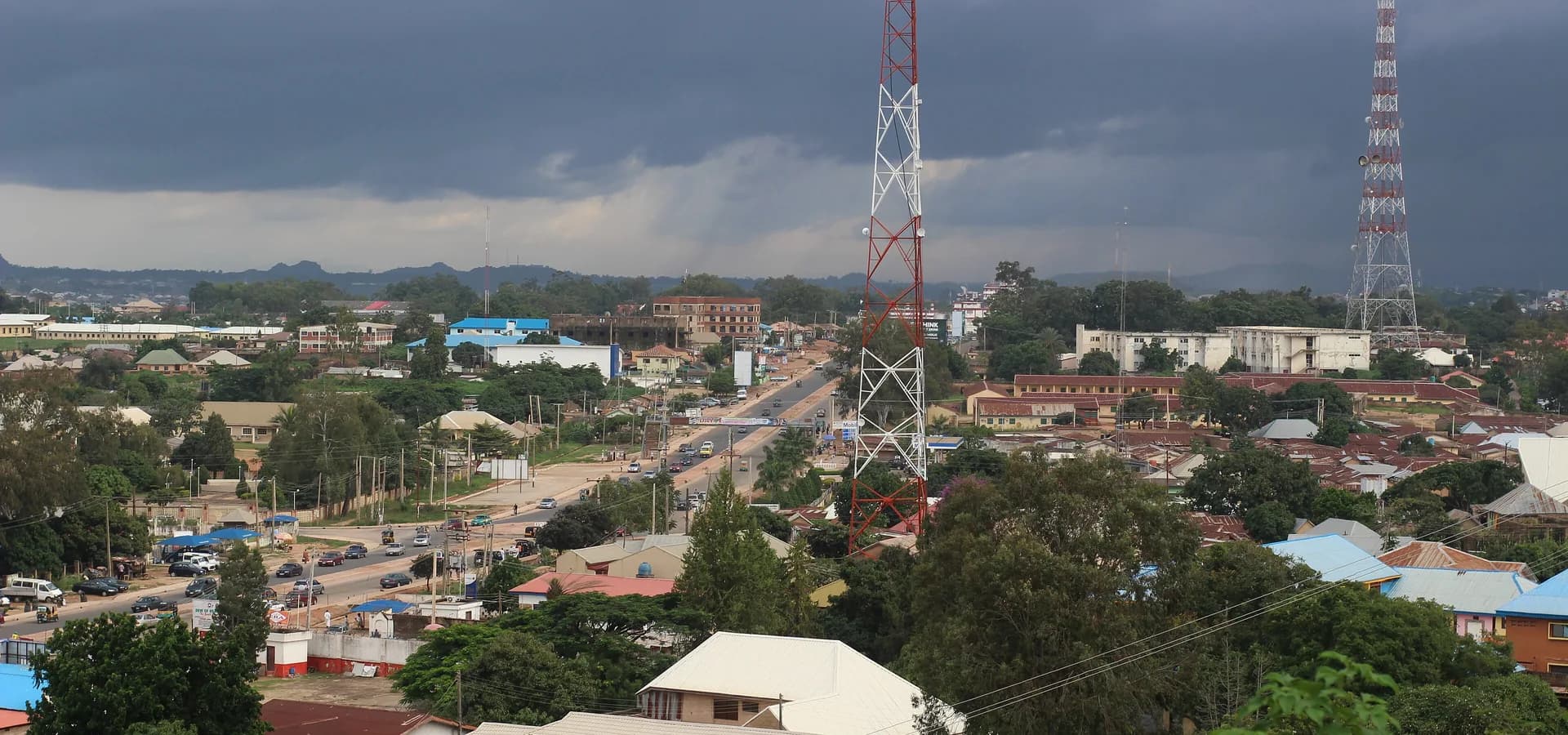 Vista al sur sobre Jos desde Anglo-Jos, con la autopista entre tejados y árboles bajo densas nubes de lluvia