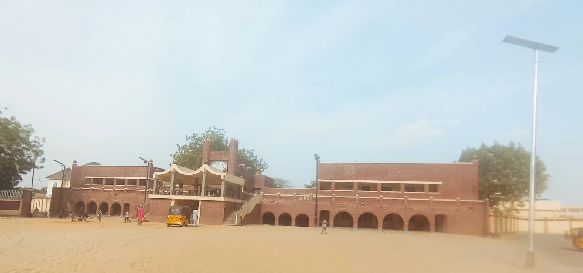 The red-brick Shehu of Borno's palace with arcades and a clock tower facing a wide sandy square