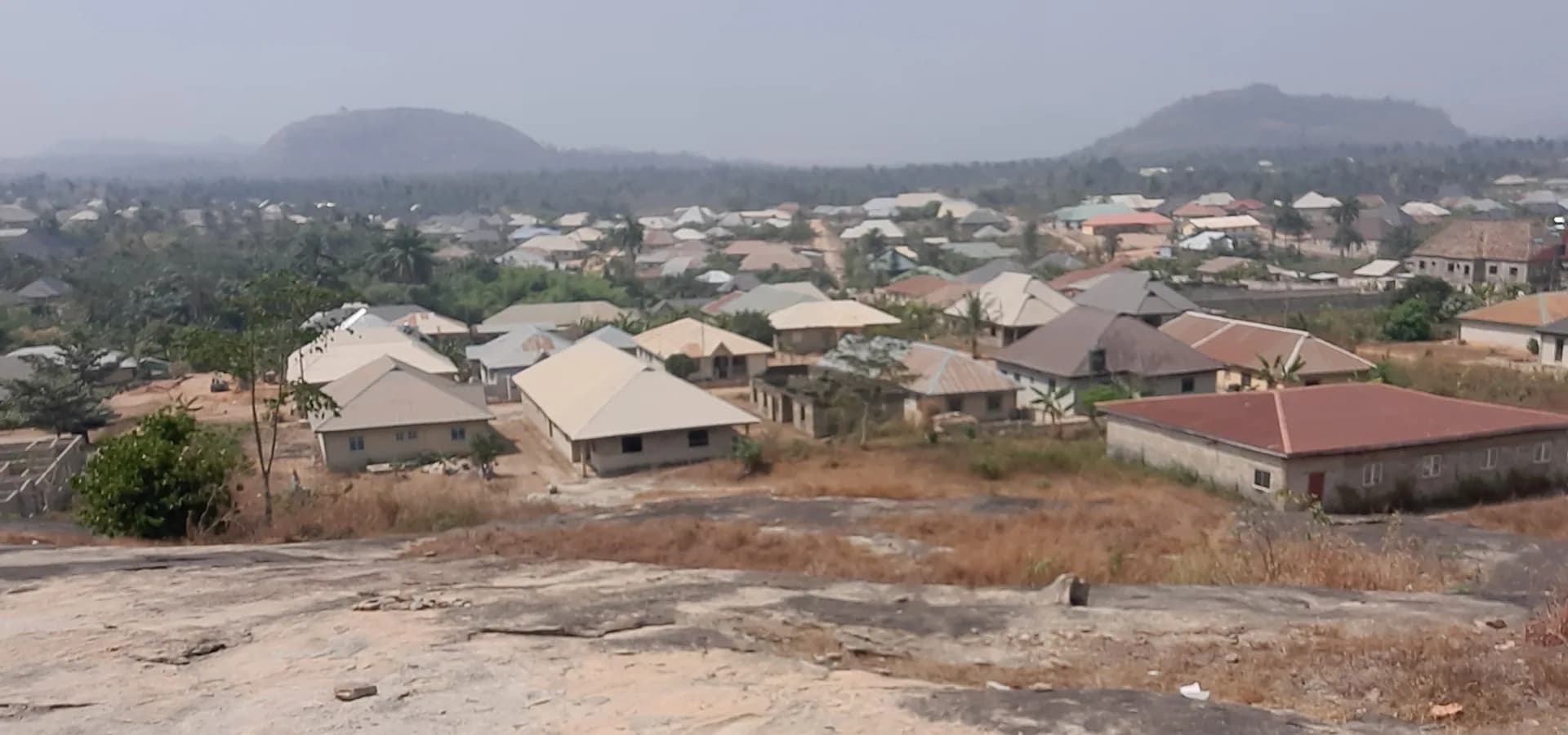 Tejados de Ondo entre palmeras hacia dos colinas boscosas bajo un cielo brumoso, vistos desde la colina Pele.