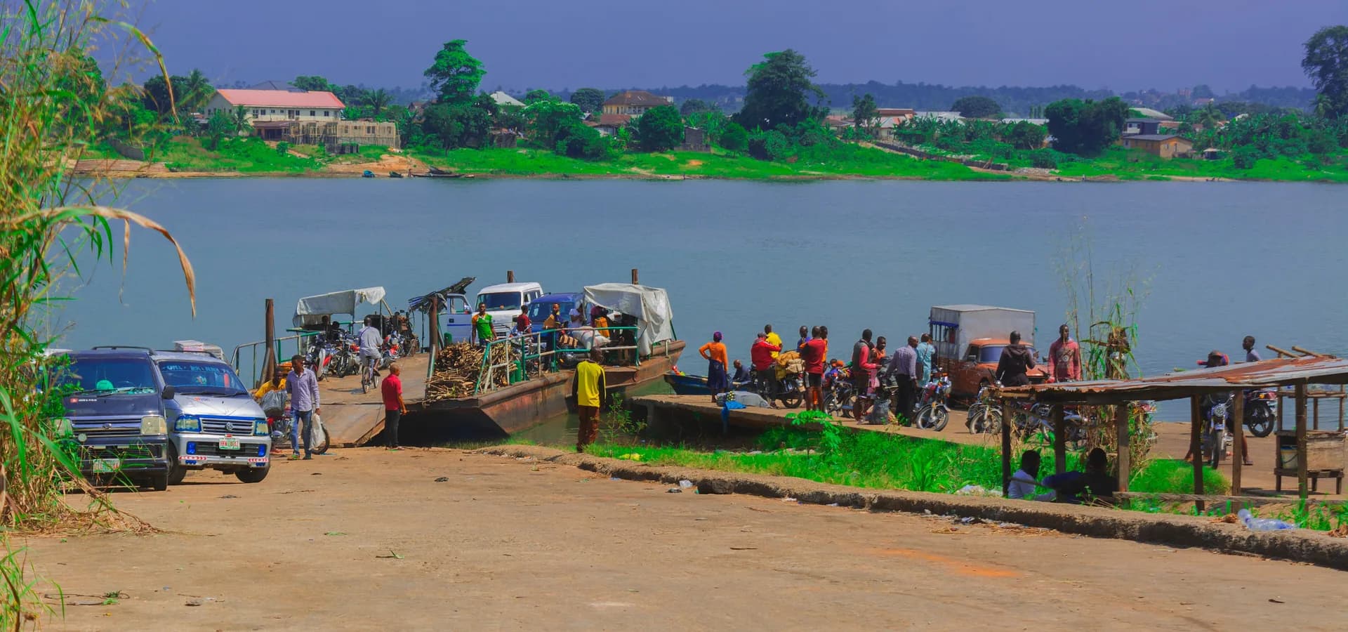 Fähranleger am Oguta Lake bei Owerri, kleine Gestalten am Wasser und dahinter ein grünes Ufer