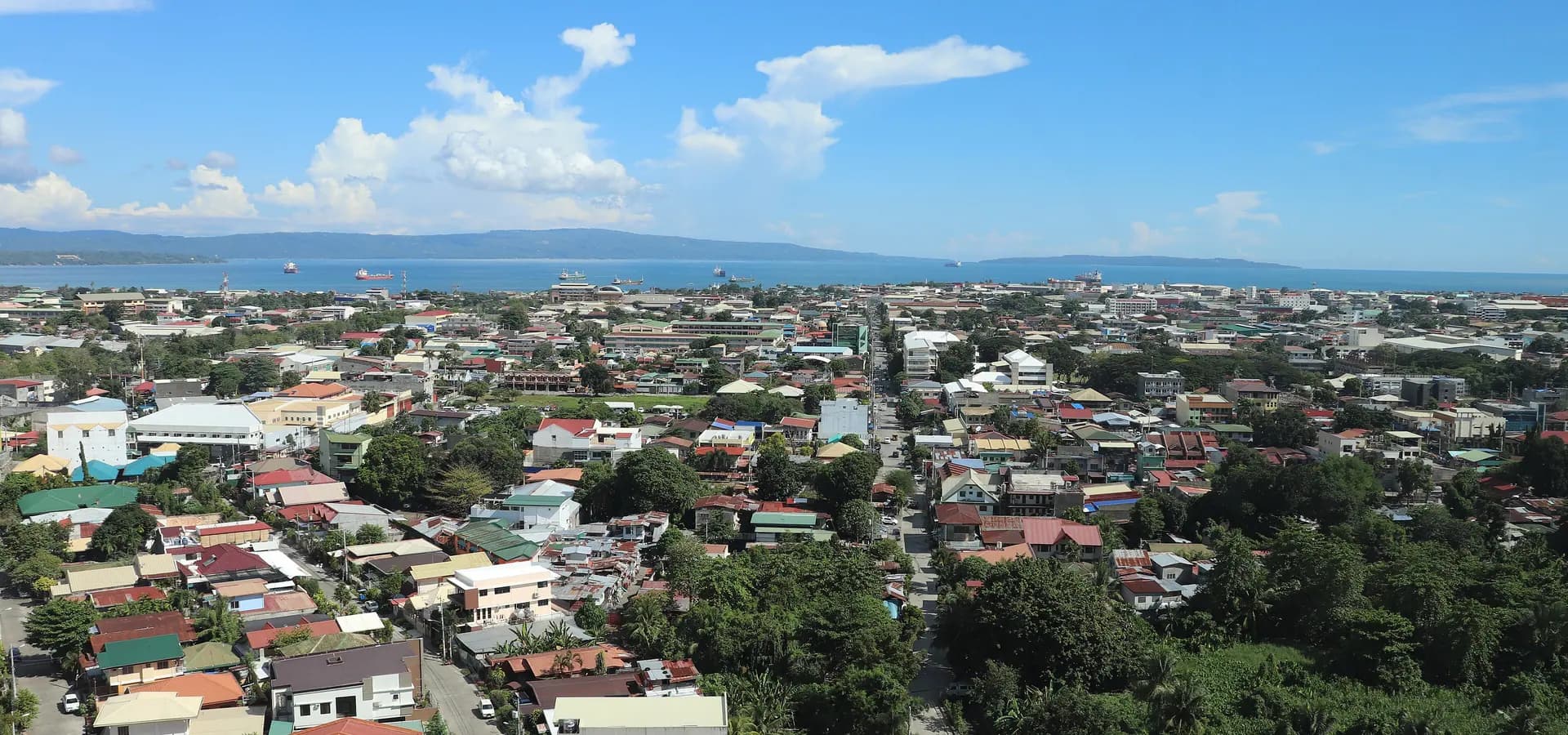 Tejados y palmeras de Davao City que se extienden hasta el azul golfo de Davao, con la isla de Samal bajo un cielo luminoso