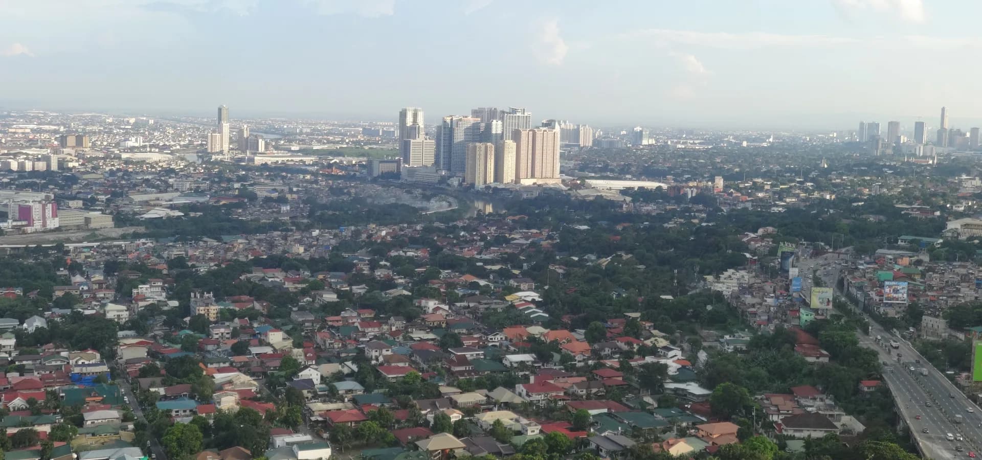Vista ampla de casas de telhado vermelho e árvores na região de Katipunan, em direção às torres do Eastwood City