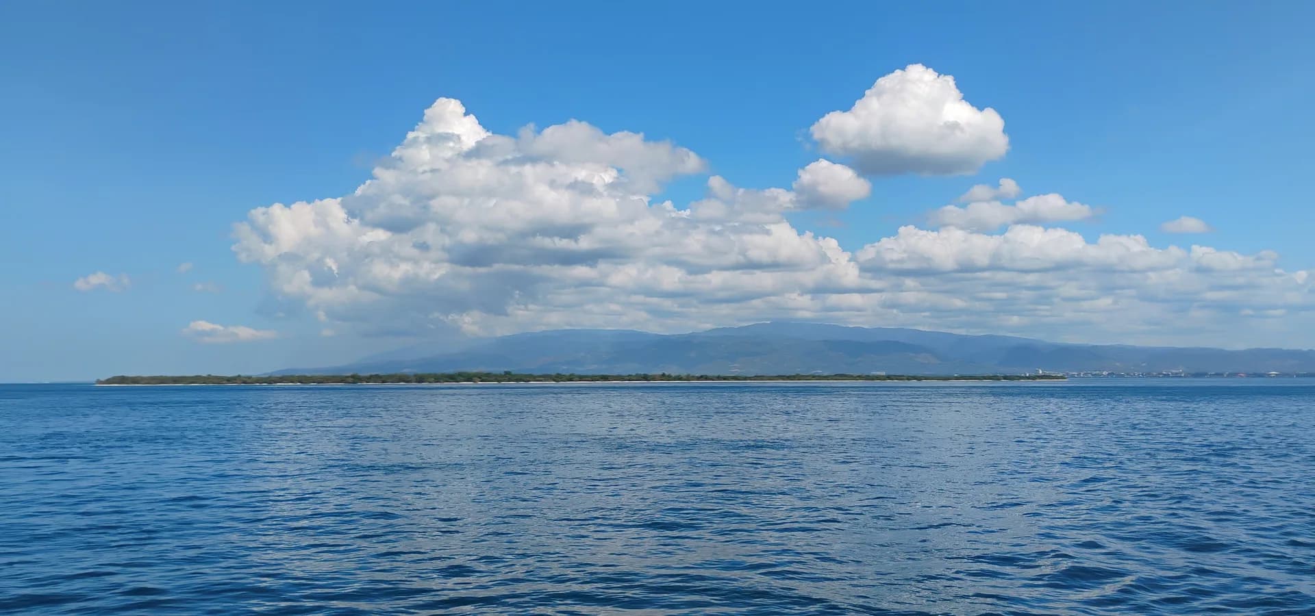Baja y verde, la Gran Isla de Santa Cruz sobre un estrecho azul y en calma, con las colinas de Zamboanga y nubes blancas detrás