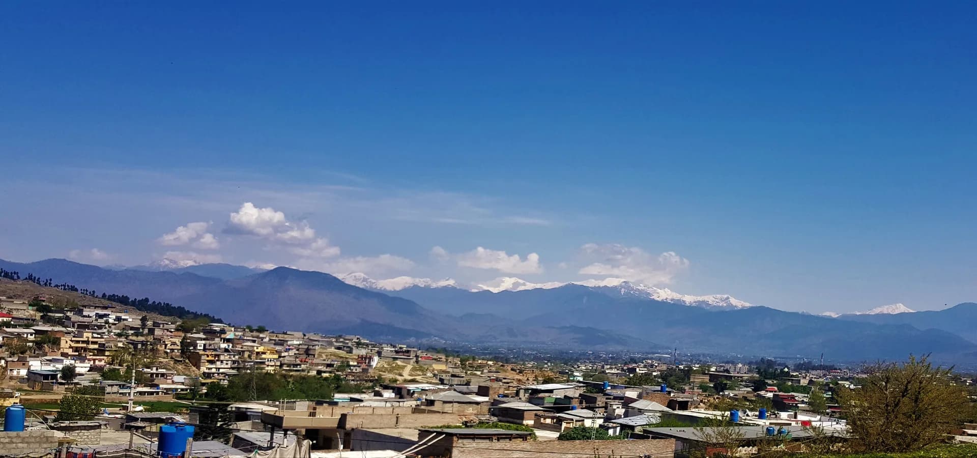 Panorama de los tejados de Abbottabad con crestas azules de montaña y picos nevados al fondo
