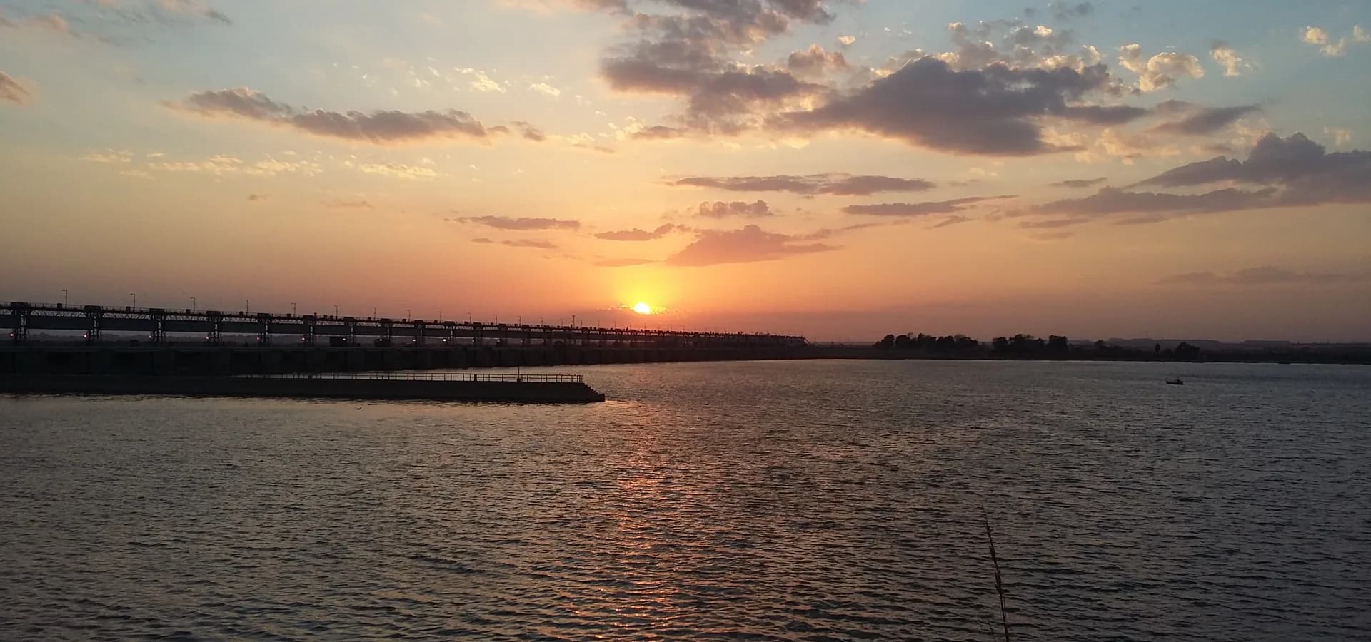 Oranger Sonnenuntergang über dem breiten Indus am Kotri-Staudamm bei Hyderabad, links der lange Staudamm