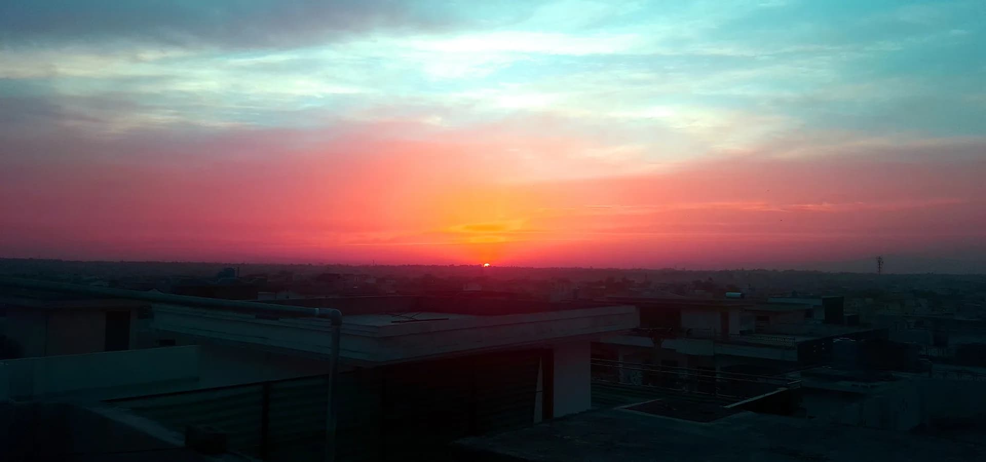 Un cielo de atardecer naranja y rosa sobre los techos planos de Rawalpindi que se extienden hasta el horizonte