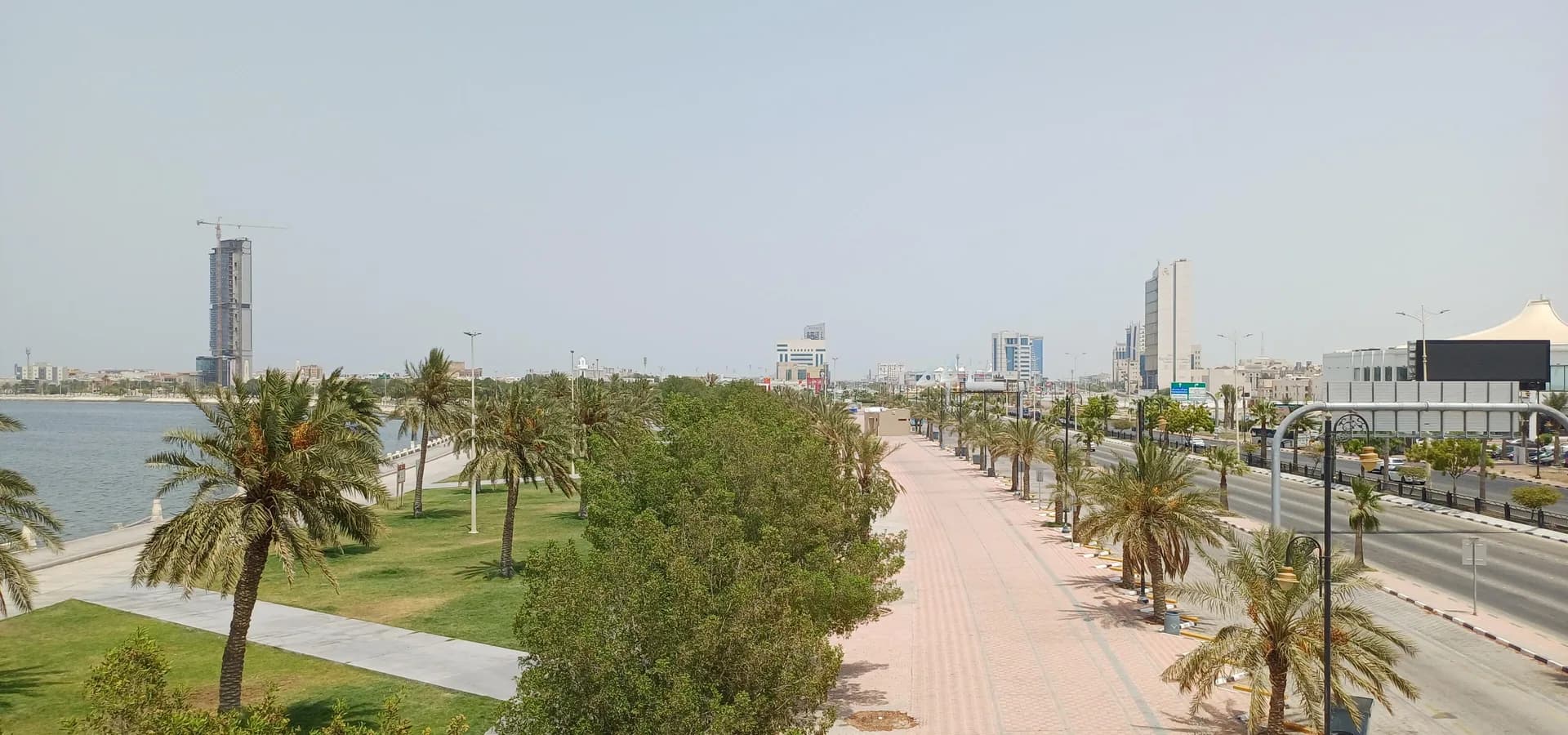 Palmengesäumte Promenade und Rasenflächen am Golf an der Dammam Corniche, mit Hochhäusern am Horizont
