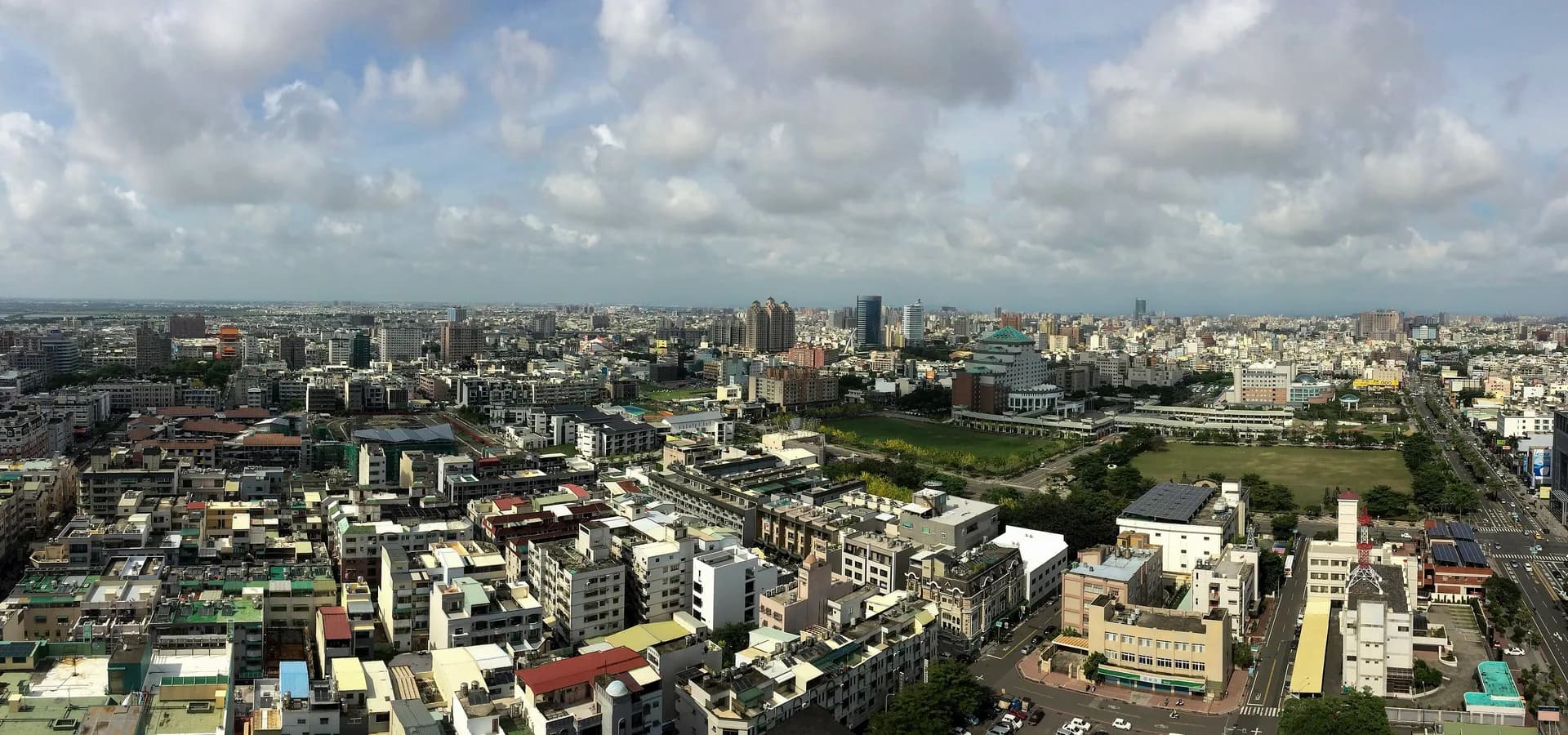 Wide daytime view over the low rooftops, towers and green parks of central Tainan under a cloudy sky