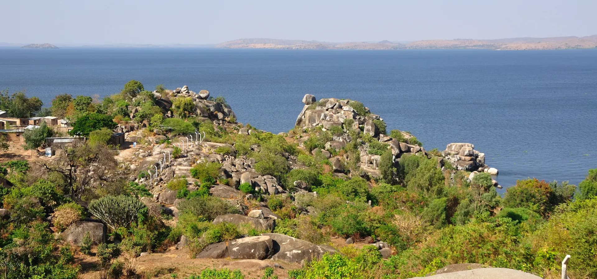 Rocky granite outcrops and green bushes on the Mwanza shoreline above the wide blue water of Lake Victoria