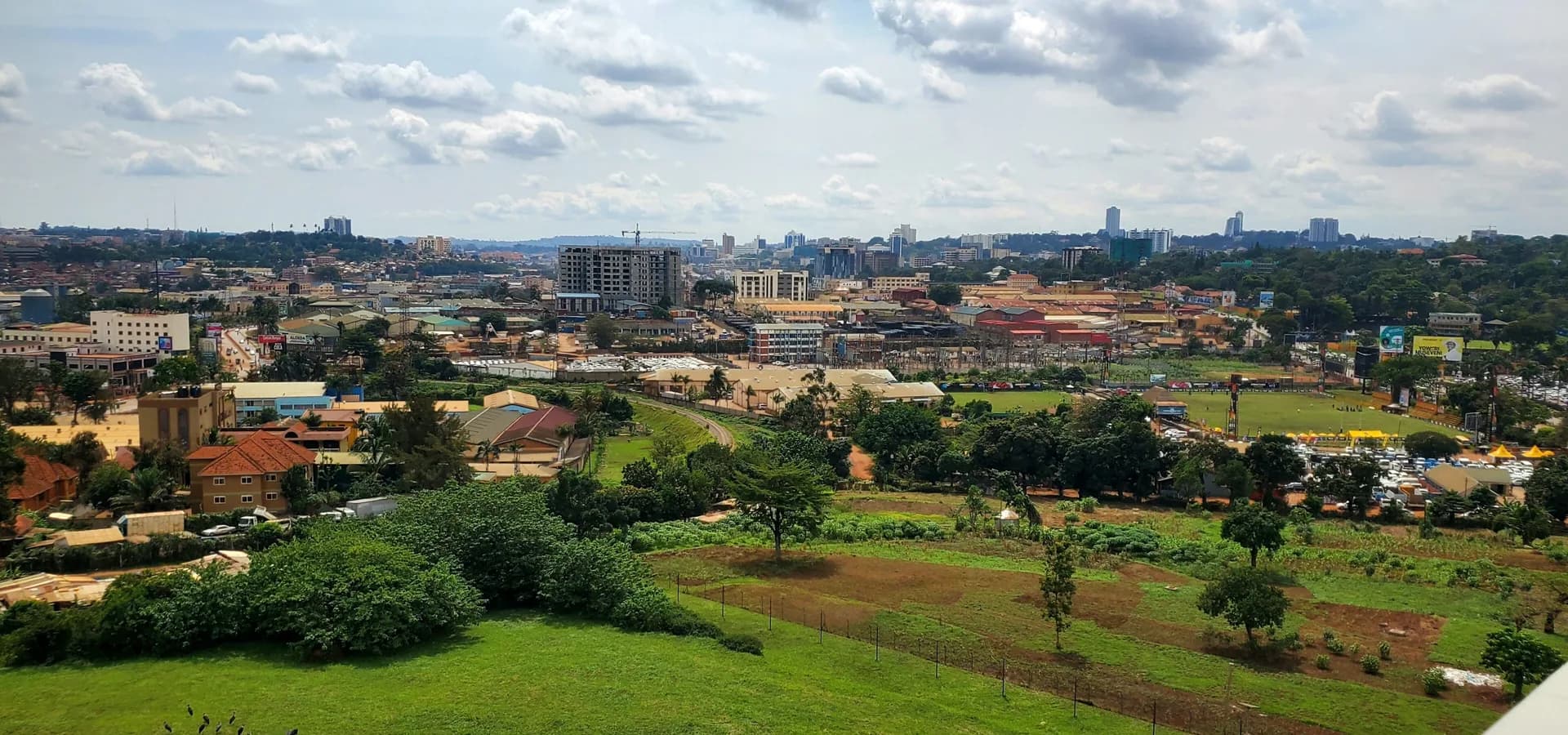 Grüner Hang und rot gedeckte Viertel, die sich unter weißen Wolken zur Hochhaus-Skyline von Kampala erstrecken