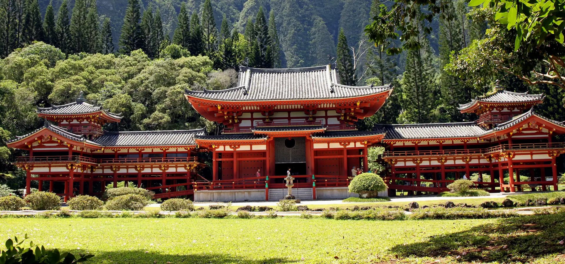 Templo Byodo-In num gramado verde, com pinheiros e os íngremes penhascos verdes de Koʻolau se erguendo atrás