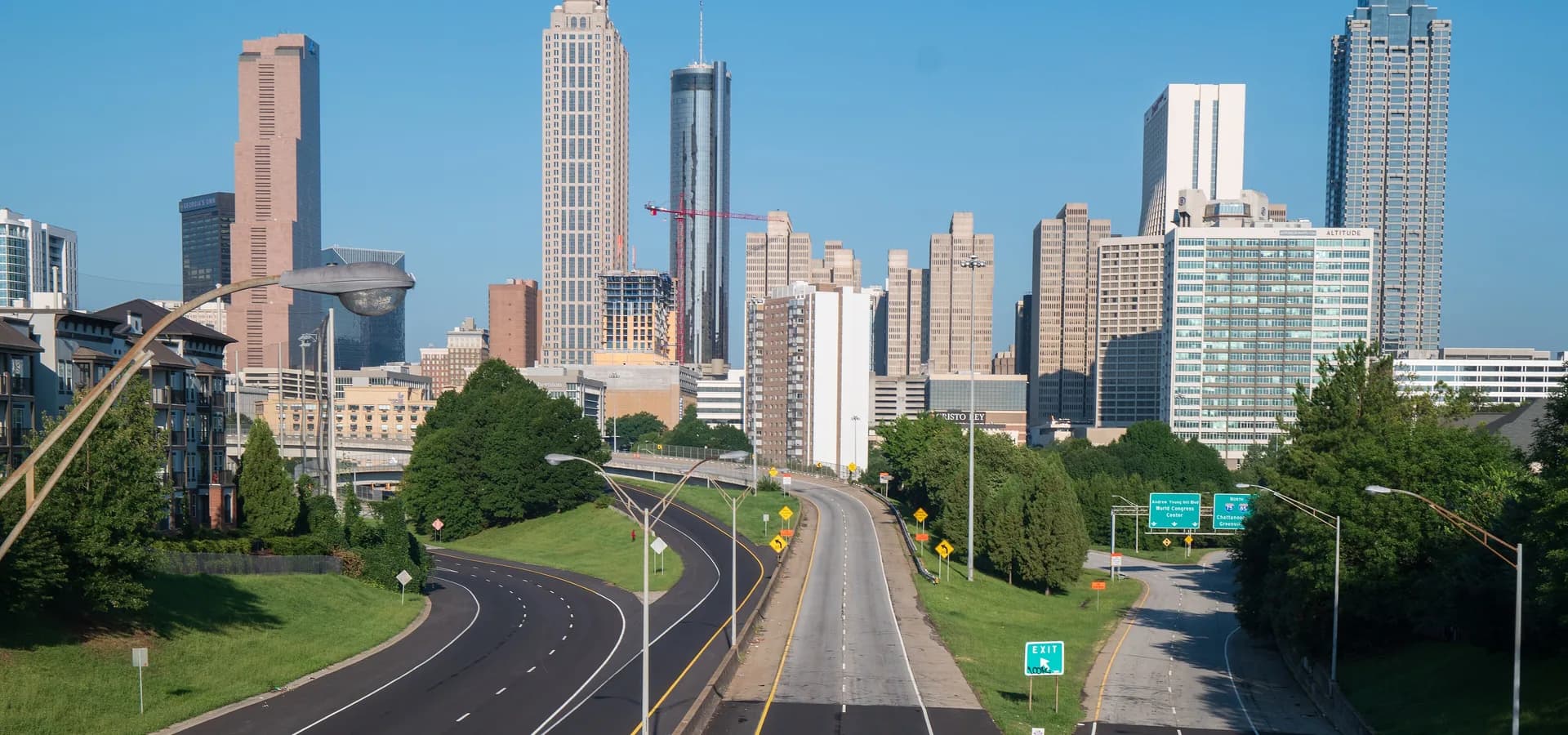 El horizonte del centro de Atlanta bajo un cielo azul despejado, con calles curvas vacías y árboles verdes desde el puente Jackson Street