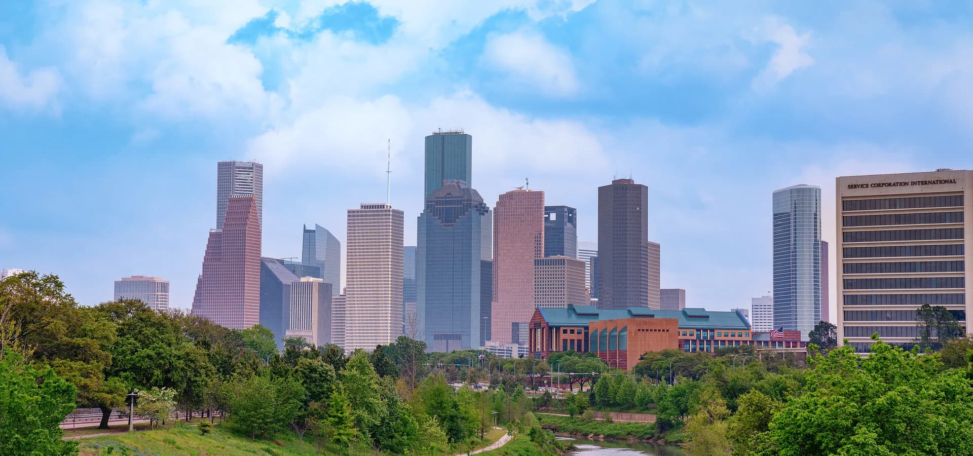 El horizonte del centro de Houston bajo nubes suaves, con el Buffalo Bayou serpenteando entre parques verdes abajo