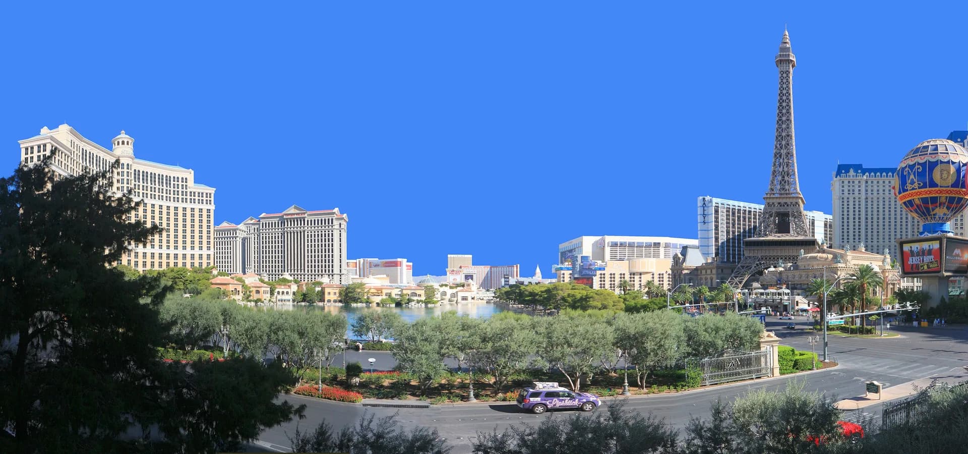 Panorama des Las Vegas Strip mit dem See des Bellagio, Palmen und dem Paris-Turm unter klarem blauem Himmel