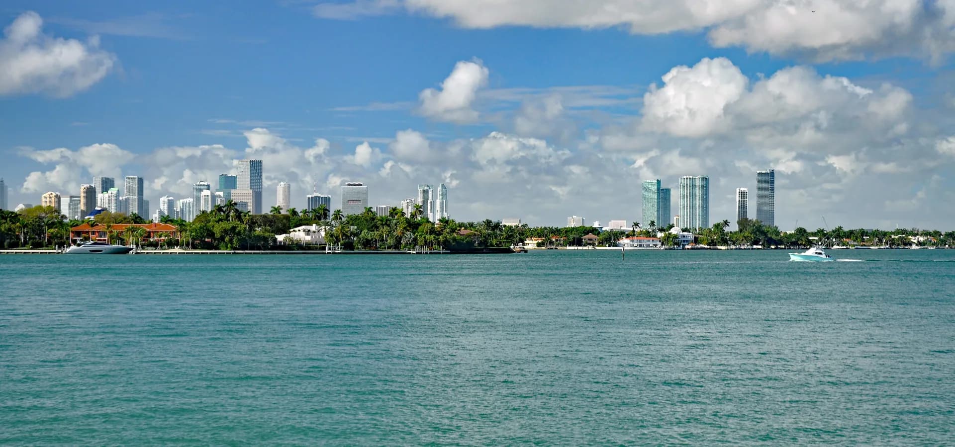 Türkisfarbenes Wasser der Biscayne Bay mit palmengesäumten Ufern und der Skyline von Miami unter weißen Quellwolken