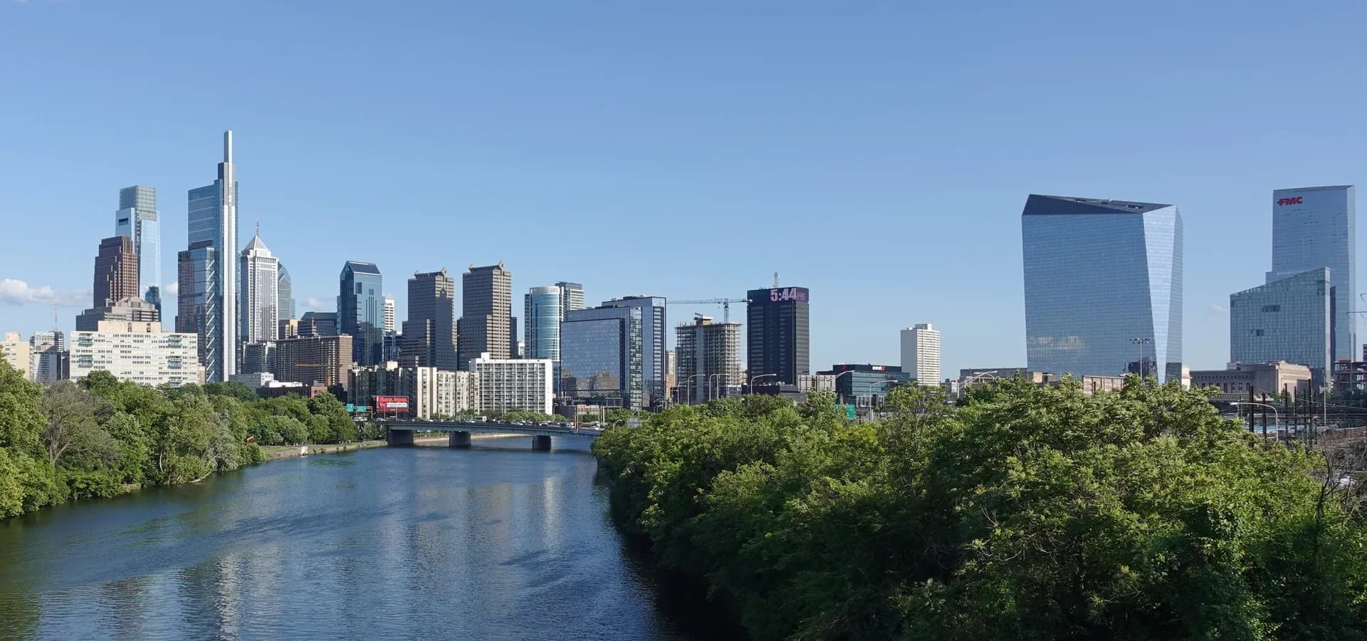 Die Skyline von Philadelphia über dem Schuylkill River, mit grünen Ufern und weitem blauem Himmel
