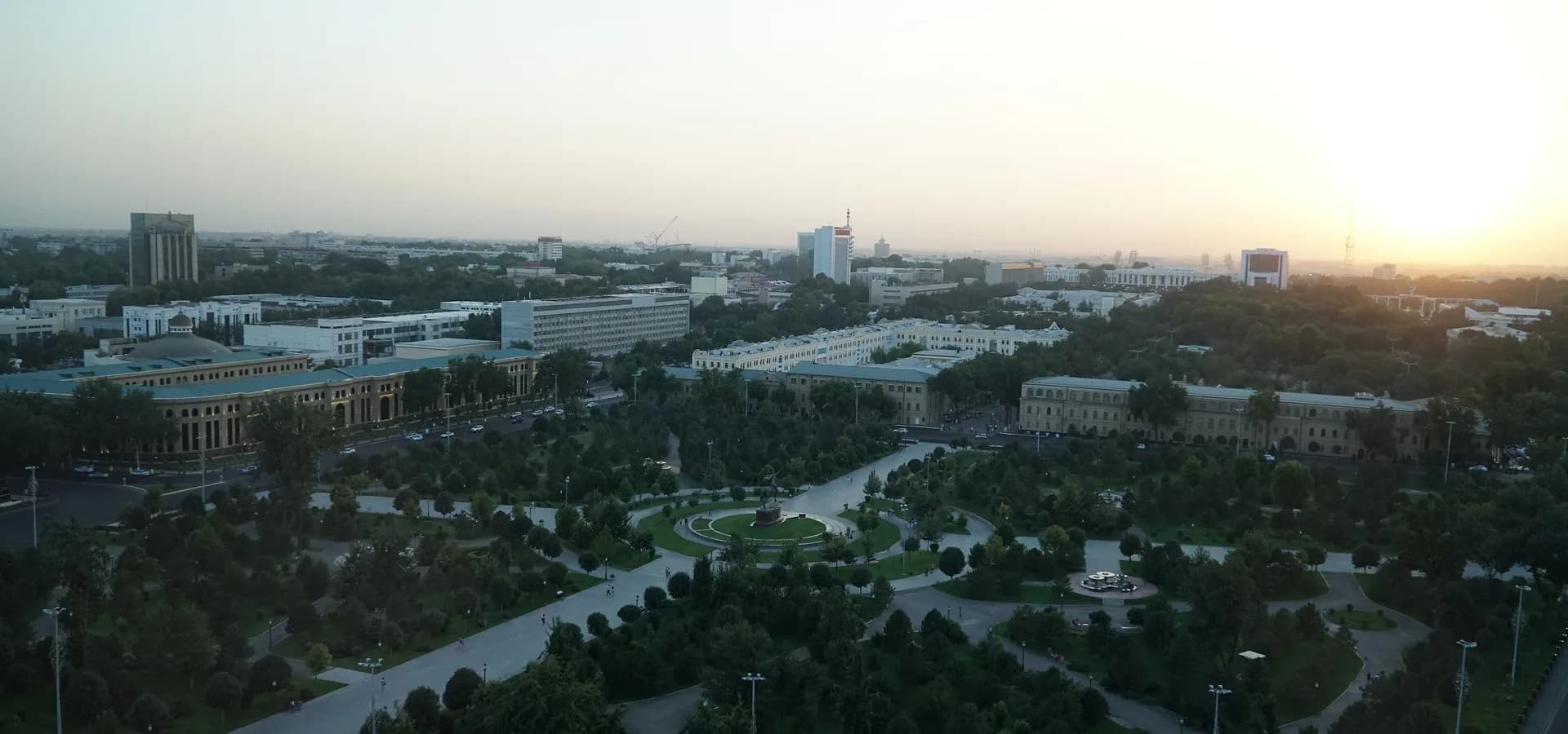 Leafy Amir Timur Square and low city buildings of central Tashkent seen from above in hazy golden sunset light