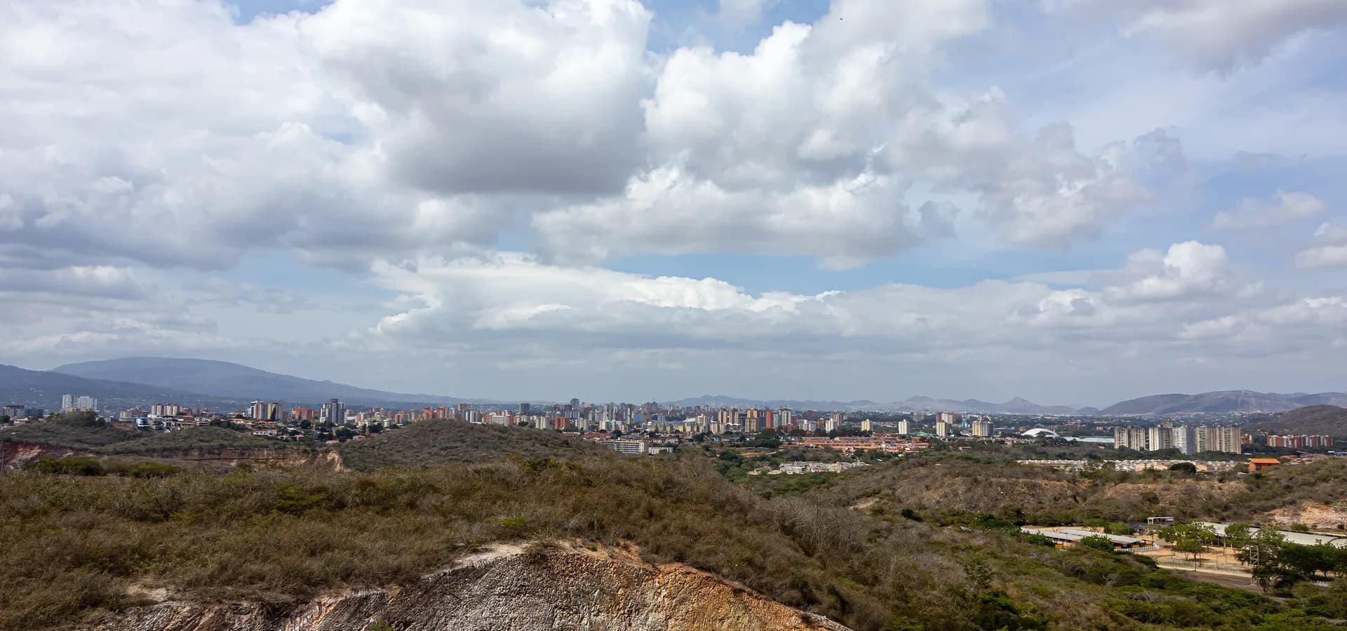 Las torres de Barquisimeto se extienden por el valle bajo colinas secas y grandes nubes blancas, con montañas en el horizonte