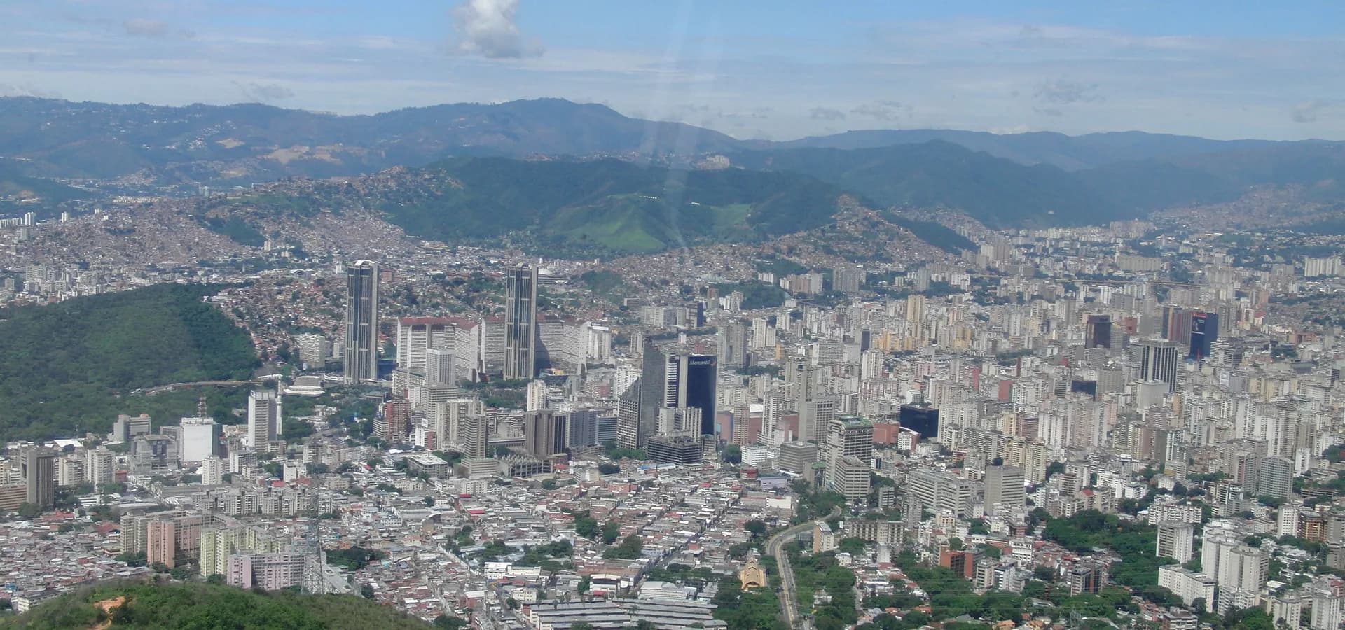El valle de Caracas lleno de edificios altos, visto desde las laderas verdes de El Ávila bajo un cielo azul.