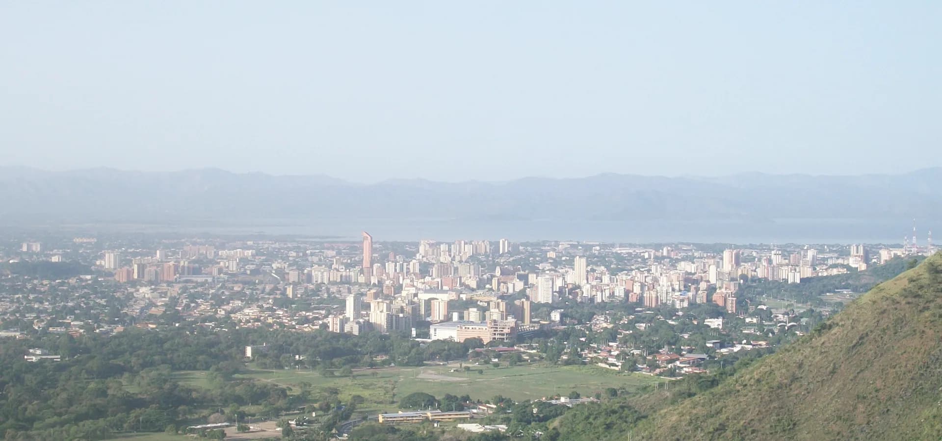 Torres de apartamentos de Maracay espalhadas por um vale verde, com o Lago de Valência e montanhas enevoadas ao fundo