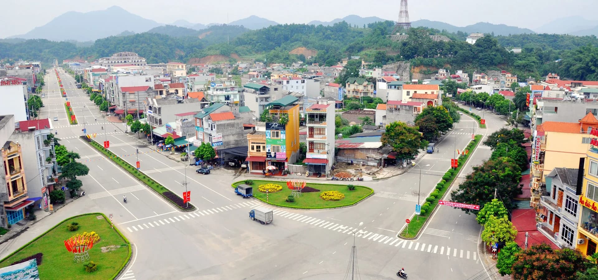 Largas avenidas e uma rotatória florida no centro de Bắc Kạn, com colinas e montanhas verdes e florestadas ao fundo