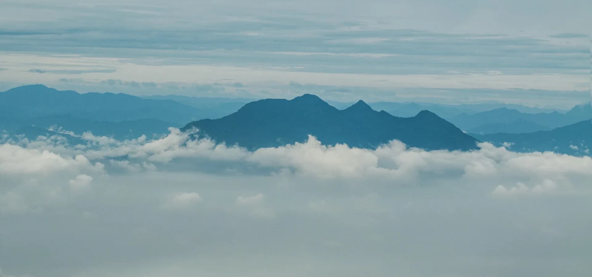 Die blauen Gipfel der Ba-Vì-Kette ragen über einer weißen Wolkenschicht unter weichem grauem Himmel auf