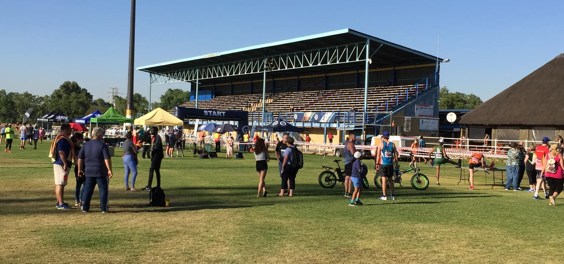 Menschenmenge auf dem Rasen vor der Tribüne des Alberton Rugby Stadium unter klarem blauem Himmel