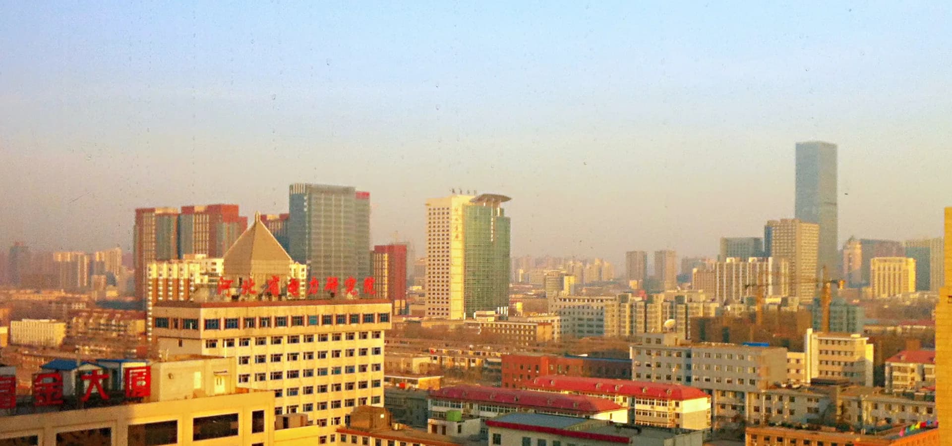 Weiter Blick über die Innenstadt von Shijiazhuang, niedrige Häuserblöcke und Glastürme unter blassem Himmel
