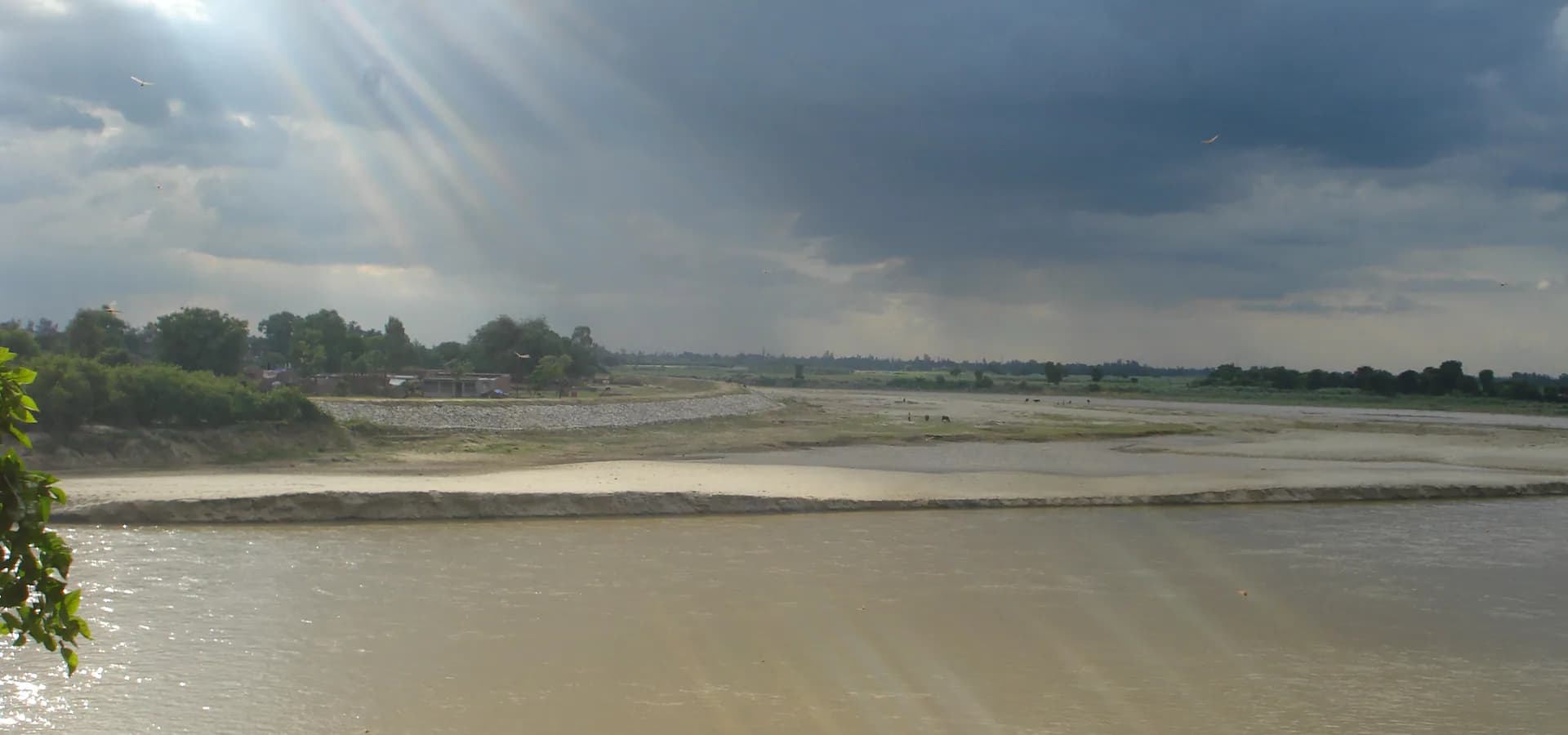 Rayos de sol entre nubes de monzón sobre el ancho río Garra y sus bancos de arena en Shahjahanpur